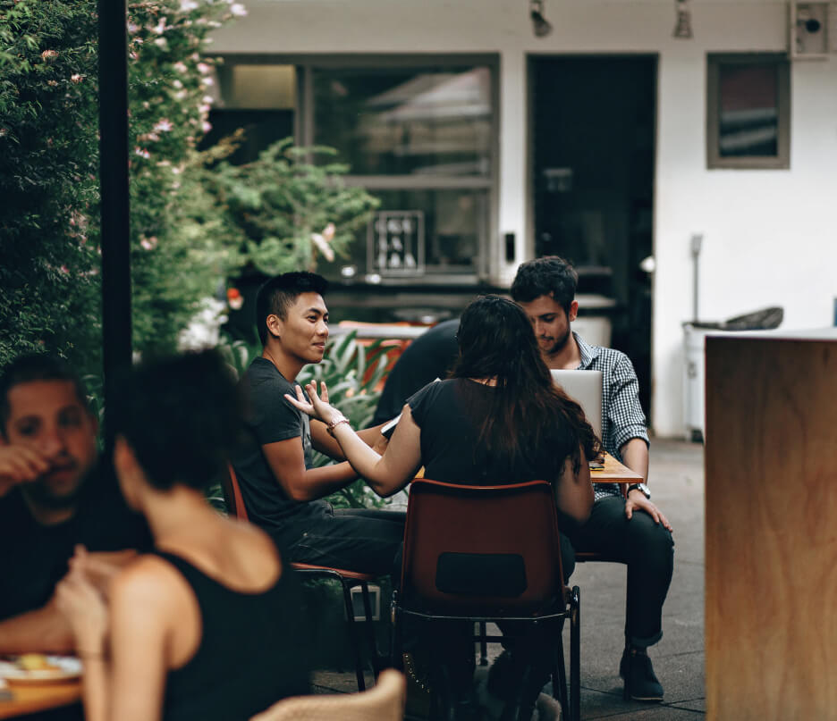 People sitting in an outdoor cafe eating and looking at their laptops