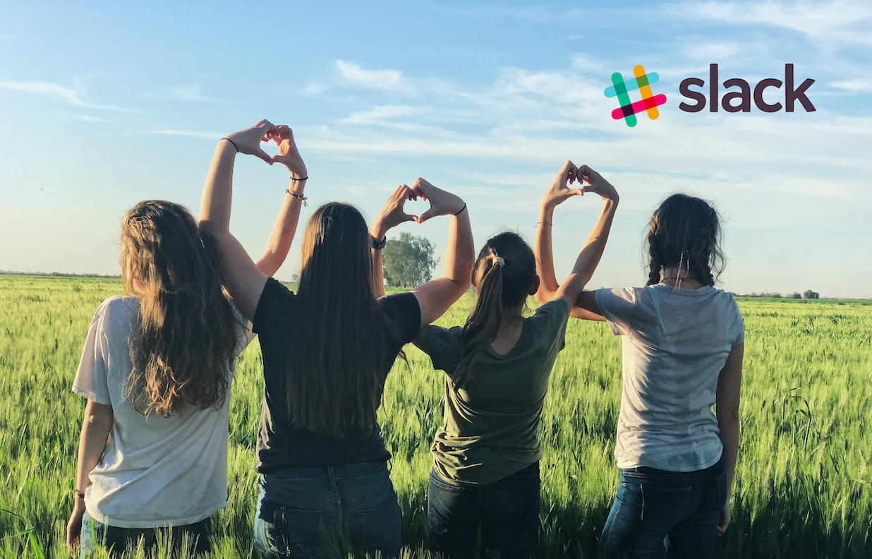 Photo of four friends standing in a field holding their hands together to form hearts with a slack logo in the top right